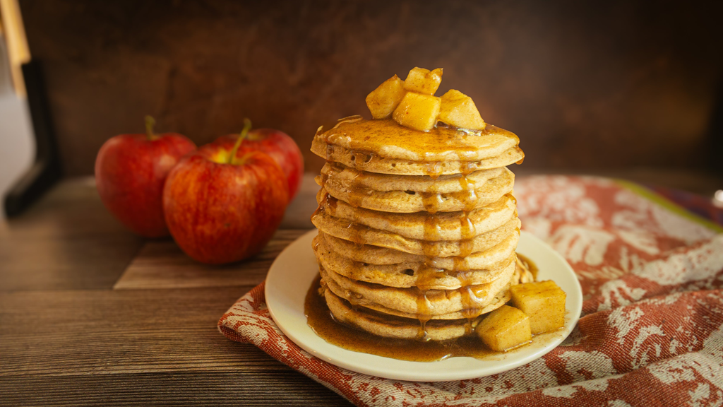 Plate with a pile of apple cinnamon pancakes topped with dripping syrup and cooked apple slices