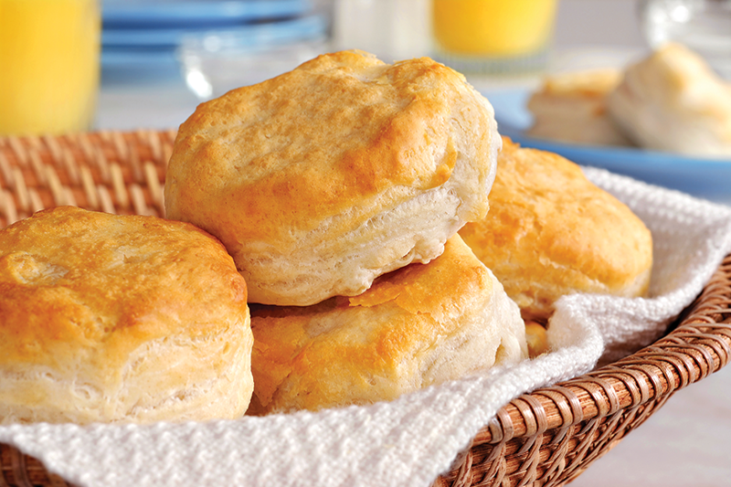 Fluffy, golden buttermilk biscuits piled up in a woven basket with a white cloth napkin