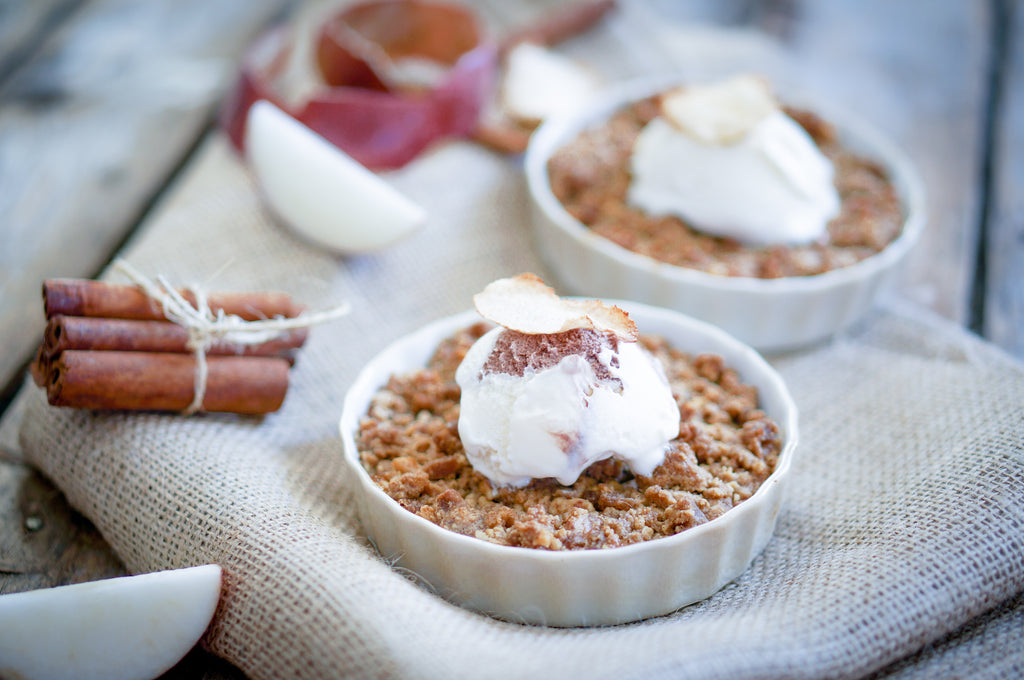 Yummy apple crisp topped with vanilla ice cream in white ramekins on a beige burlap tablecloth.