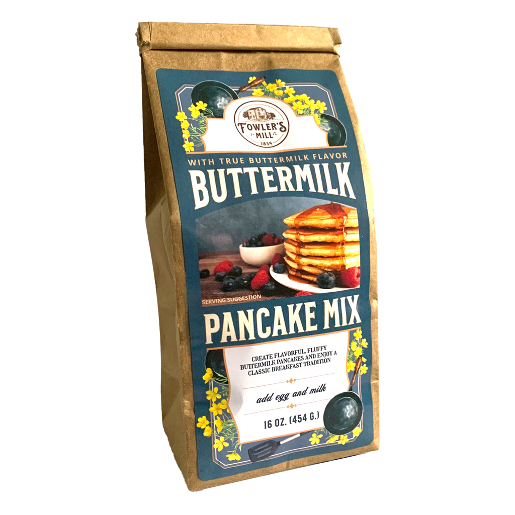 Front of Fowler's Mill Buttermilk Pancake Mix in a brown kraft paper bag with a glossy dusty blue label featuring an illustration of yellow flowers and a photo of a stack of warm pancakes.